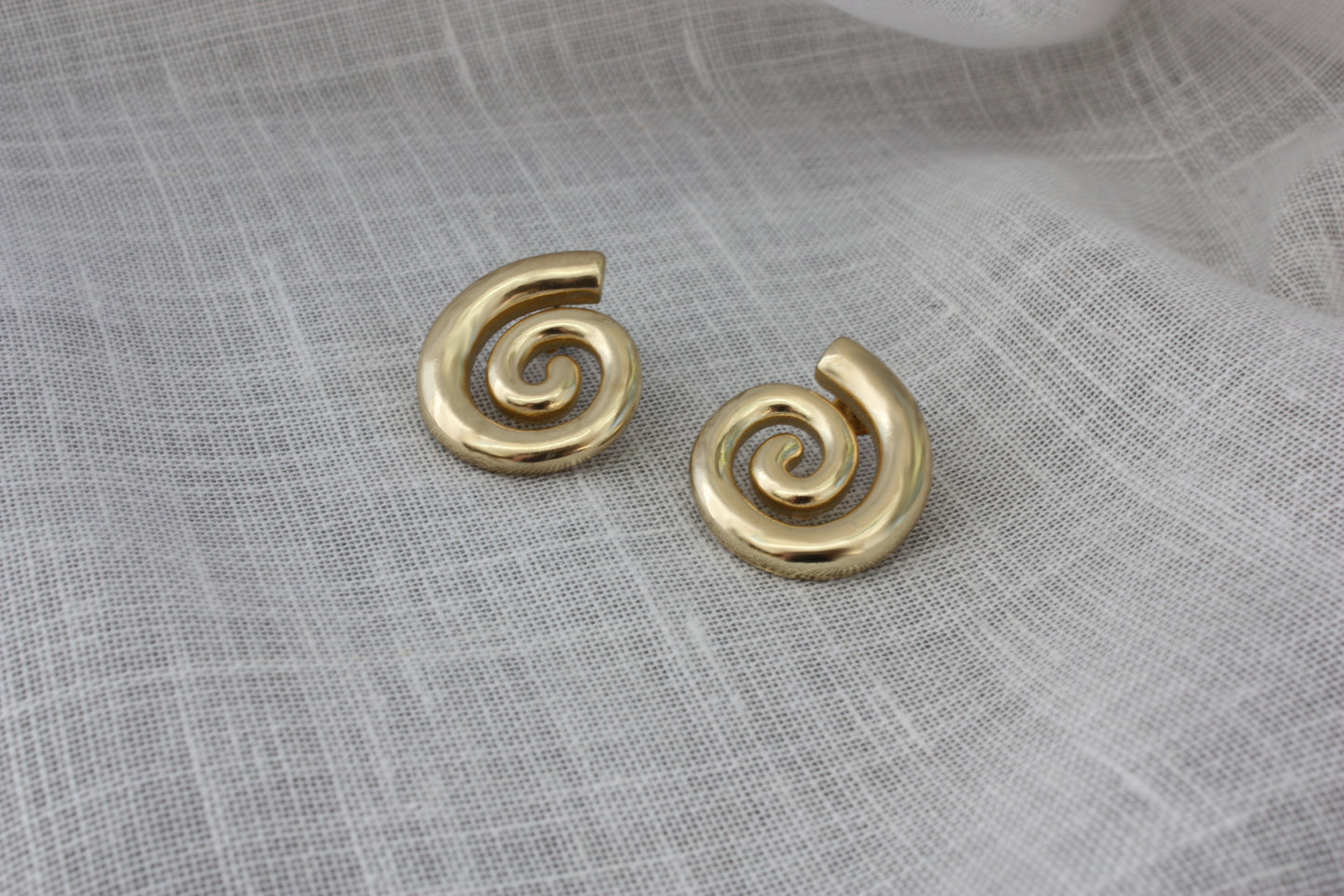 ÈRE Iris Earrings displayed on a textured surface, highlighting their elegant spiral shape. Ideal gold statement earrings for any outfit.