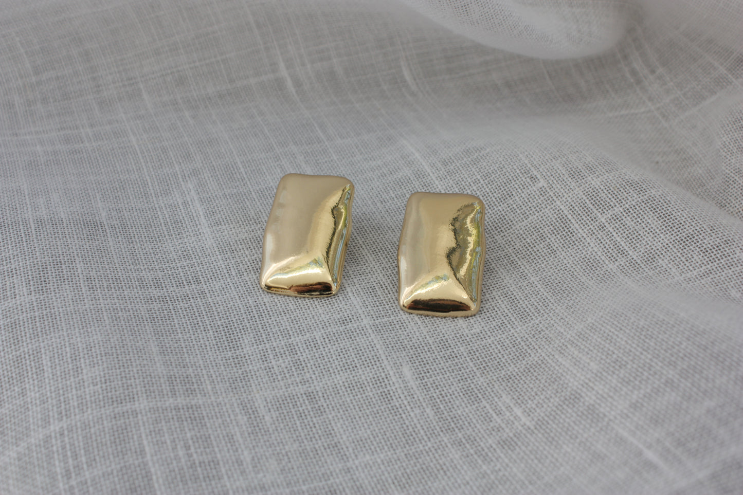 Elegant Harper Earrings from ÈRE displayed on a soft fabric, representing modern gold statement earrings with a shiny finish.