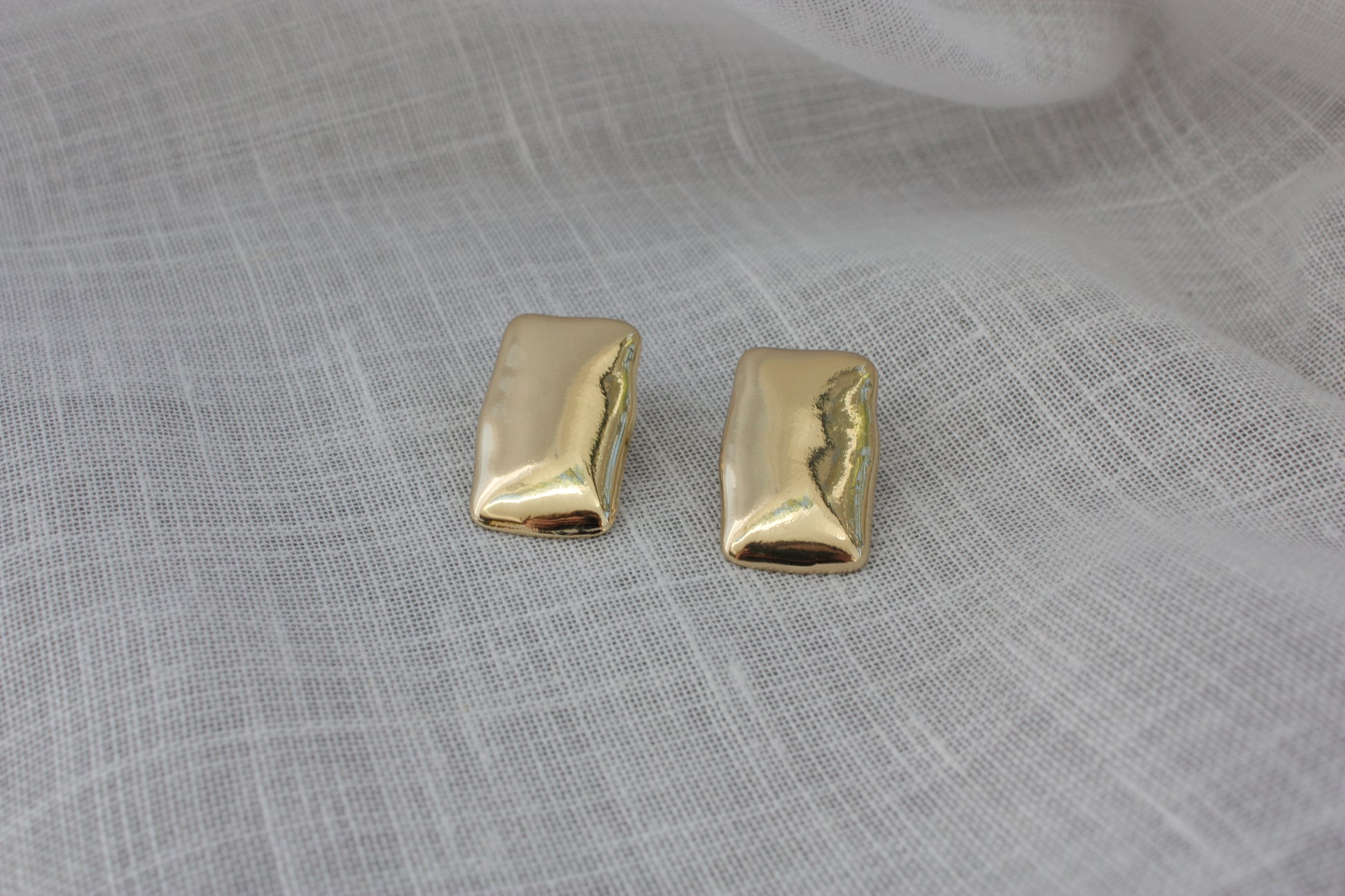 Elegant Harper Earrings from ÈRE displayed on a soft fabric, representing modern gold statement earrings with a shiny finish.