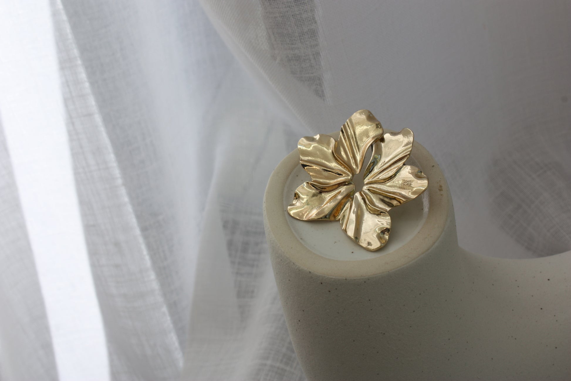 Faye Earrings by ÈRE placed on a minimalist display, showcasing their exquisite floral statement earrings design in gold.