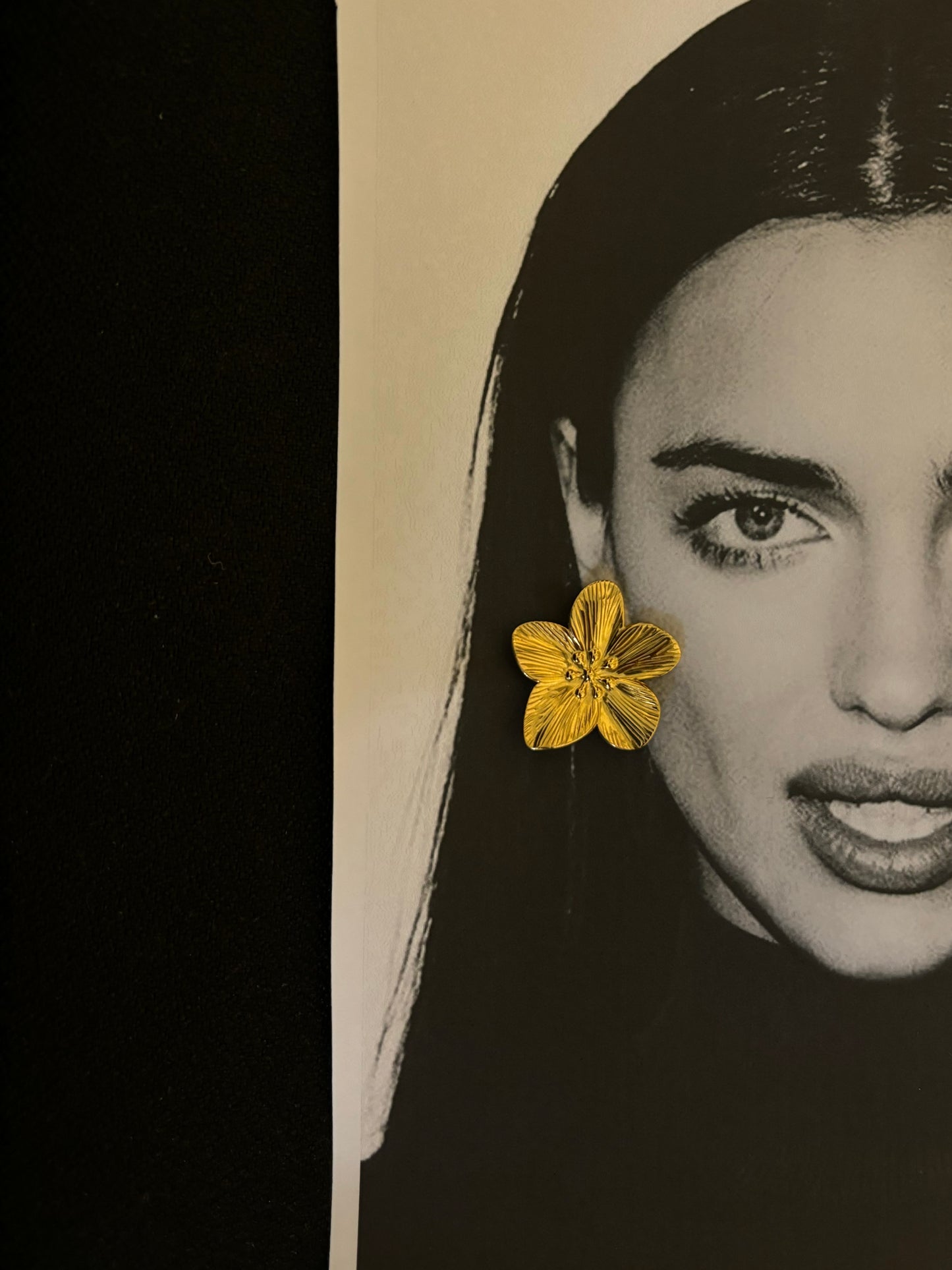 Close-up of Fleur Earrings from ÈRE placed on a black and white portrait, highlighting their golden floral design. A perfect addition among flower statement earrings.