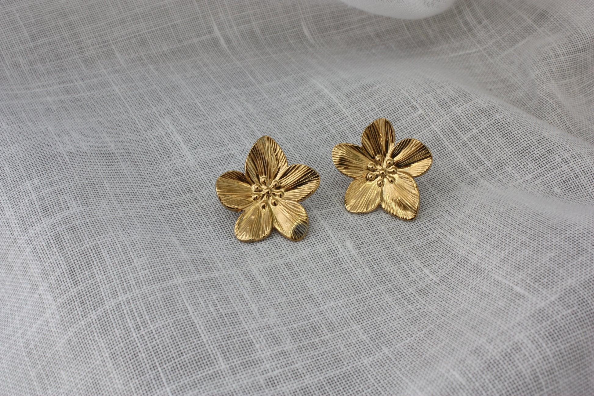 Stylish Fleur Earrings by ÈRE displayed on a soft fabric background, emphasizing their gold sheen and floral motif. Ideal flower statement earrings for a chic look.