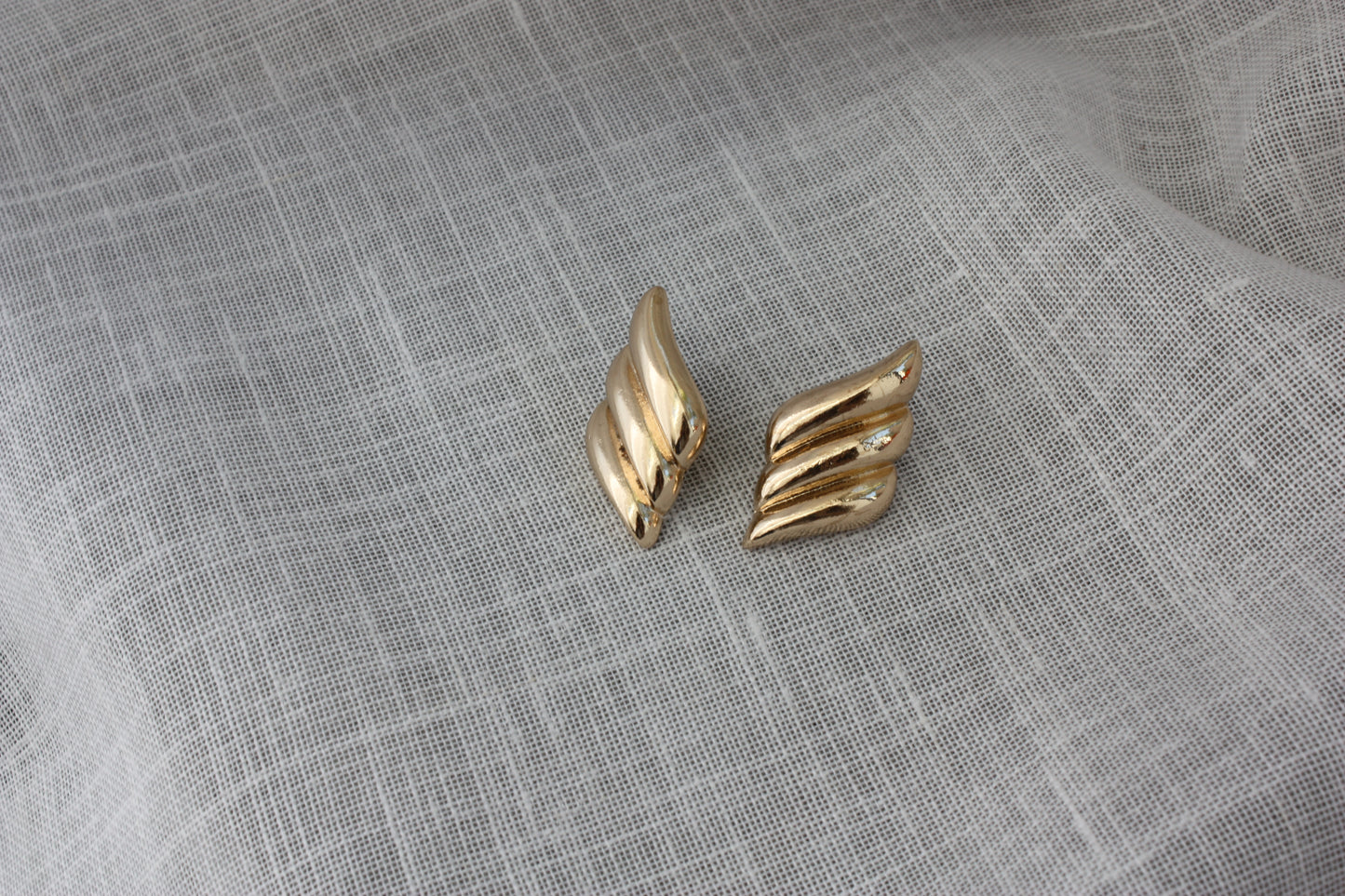 Stylish Paloma Earrings by ÈRE displayed on a soft textured surface, showcasing their intricate wing-inspired design as standout gold statement earrings.